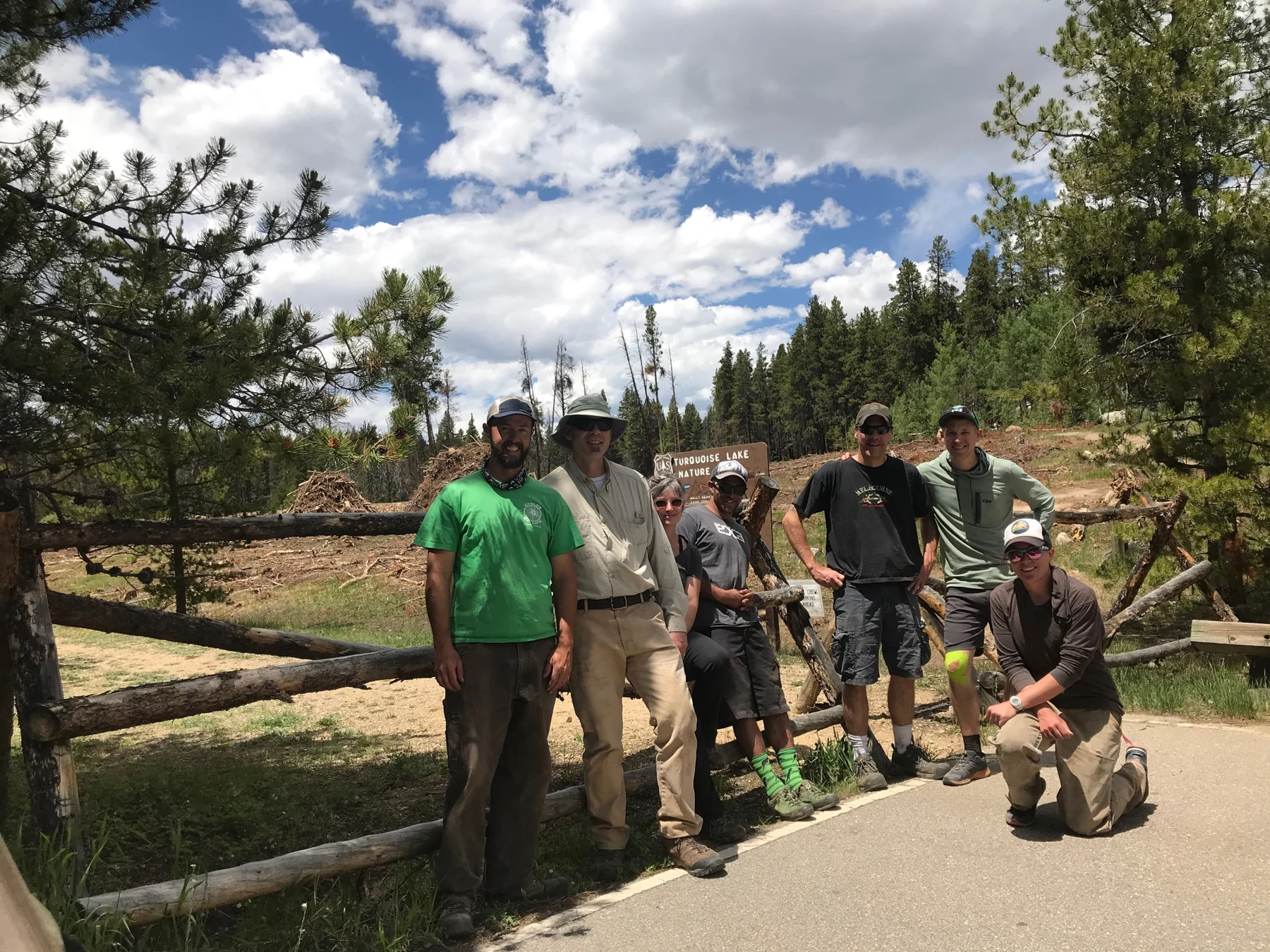 A volunteer group gathers by the Turquoise Lake Nature Trail sign beneath a cloud-filled sky.