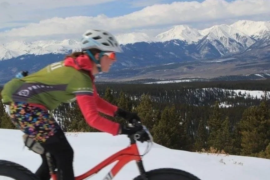 An East Side Epic rider passes across a snowy high-elevation landscape with mountains behind.